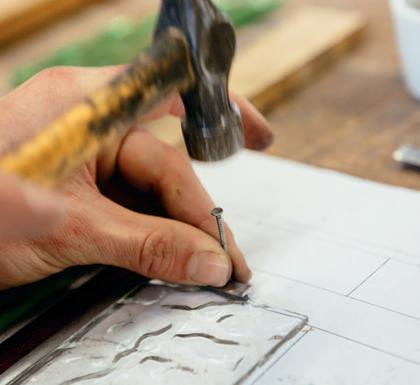 Nailing a piece of lead against a piece of glass to help keep panel pieces in place during assembly.